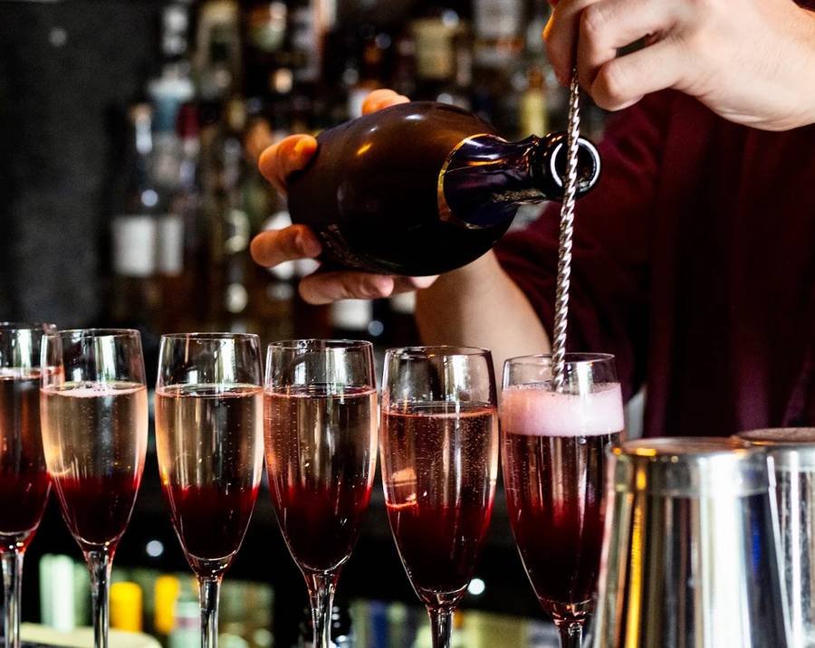 A bartender pouring a sparkling arrival cocktail into a row of flutes