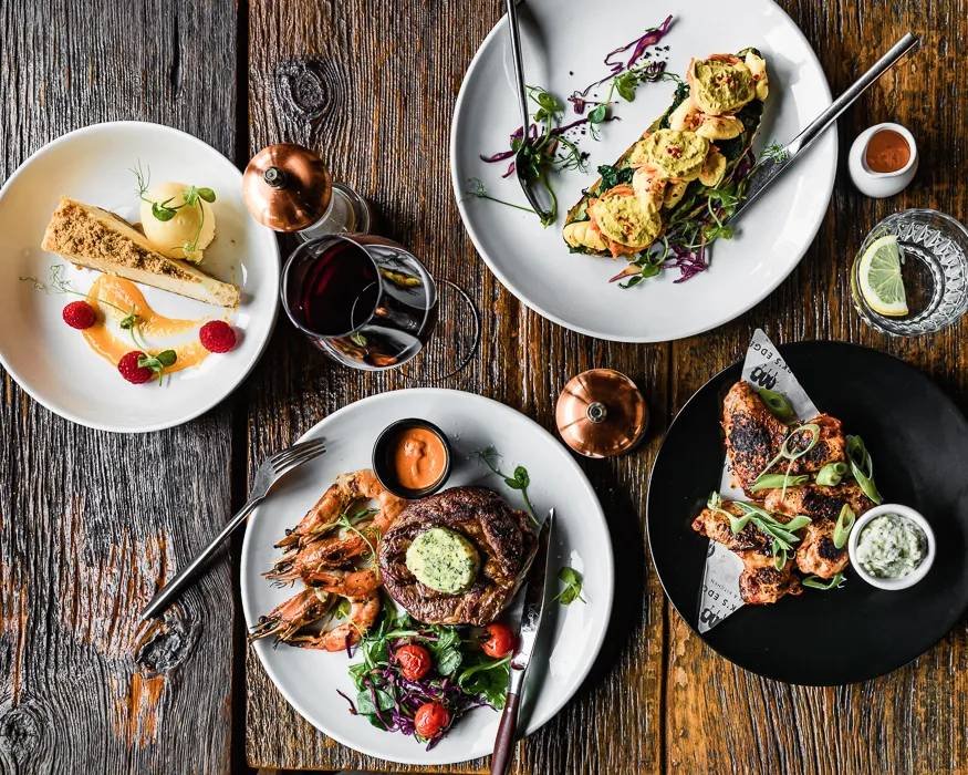 Steak, prawns, jerk chicken and dessert laid out on a wooden table